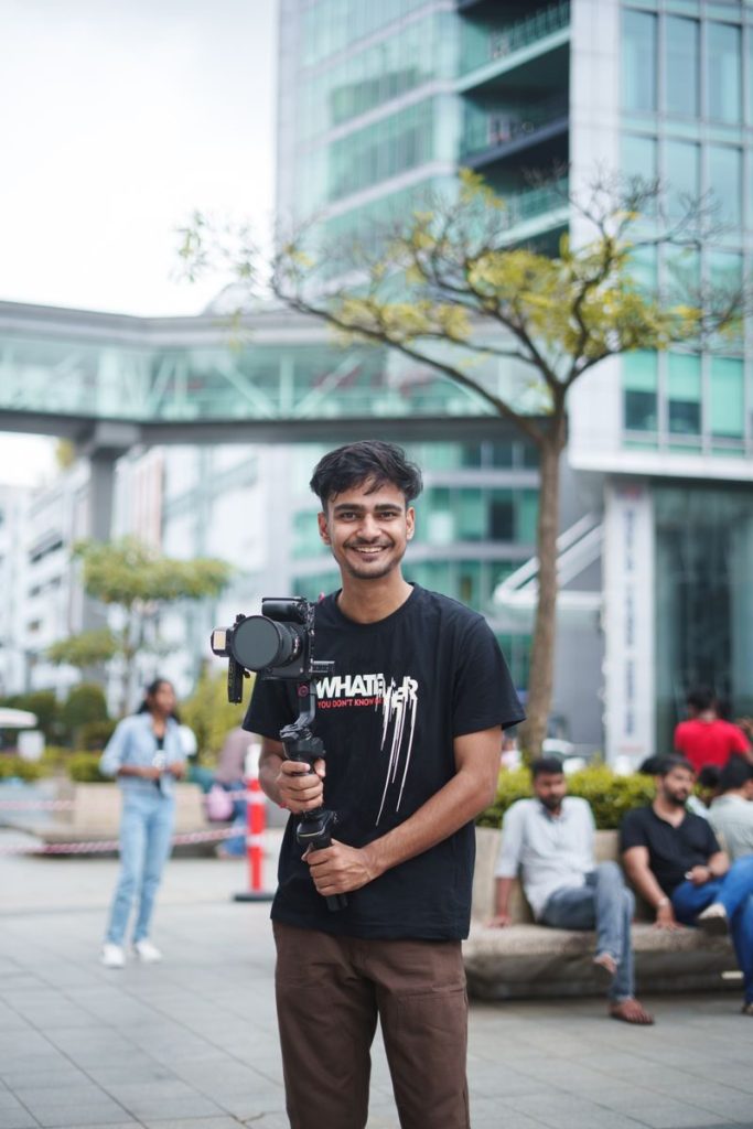 A young filmmaker smiling while holding a camera in a vibrant urban setting.